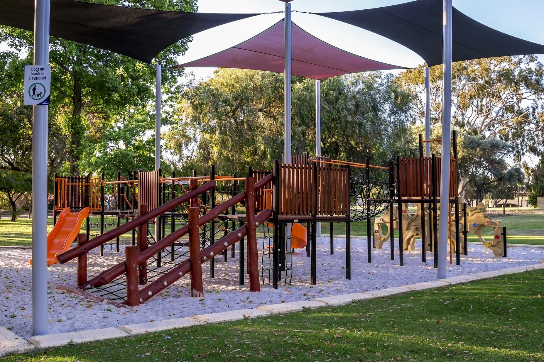 Shaded playground with climbing equipment and sand surfacing